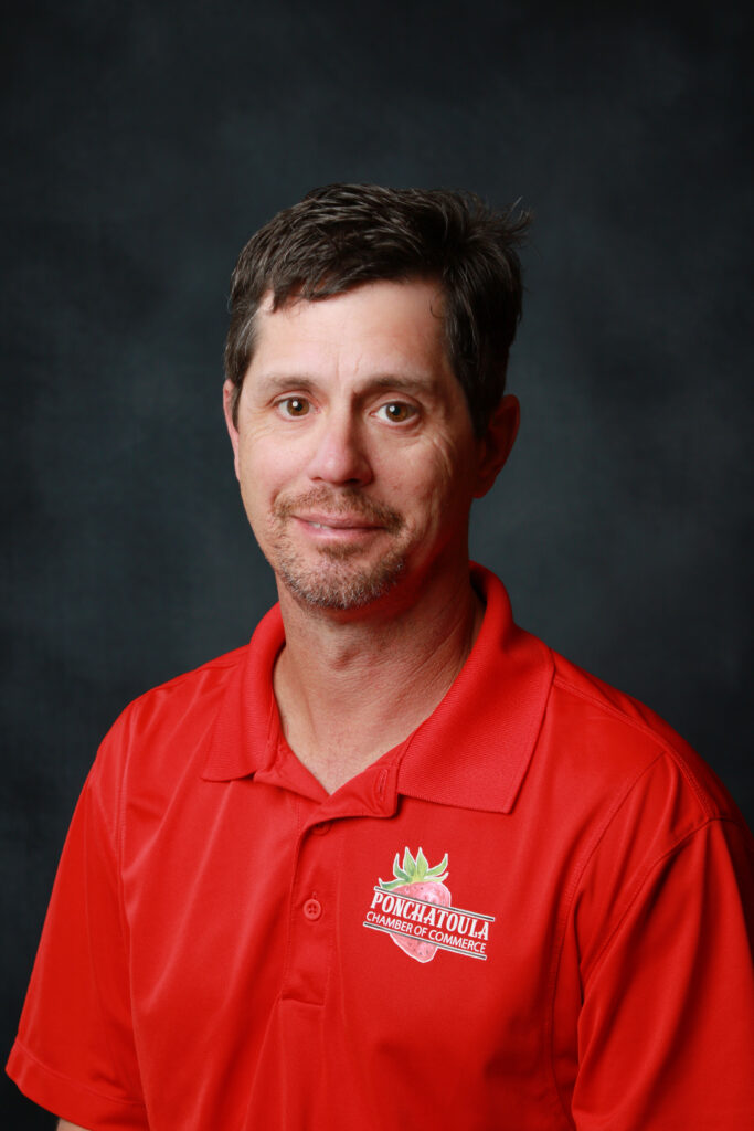 Head-and-shoulders portrait of a man in a red polo shirt with a Ponchatoula Chamber of Commerce logo against a dark background