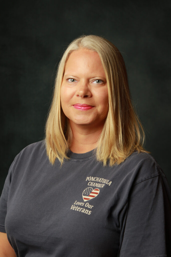 Portrait of a woman with long blonde hair wearing a dark T-shirt featuring the Ponchatoula Chamber 'Loves Our Veterans' logo with a heart-shaped American flag design.