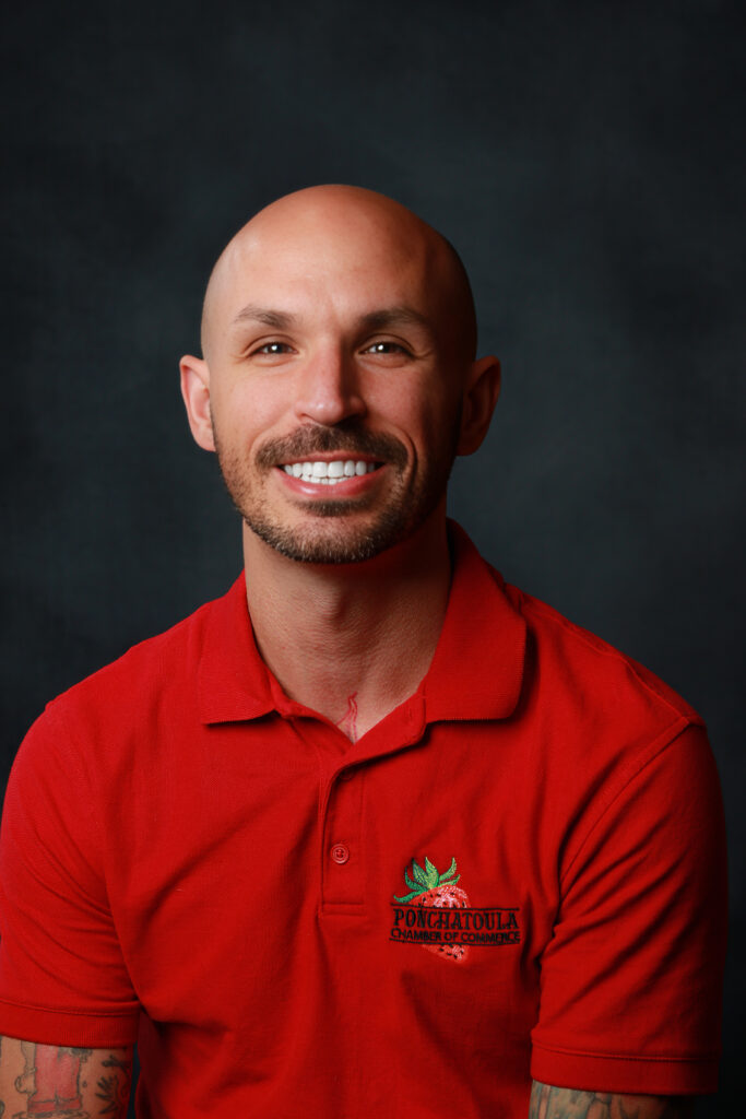 Smiling man in a red polo shirt against a dark background, logo reads Ponchatoula Chamber of Commerce on chest.