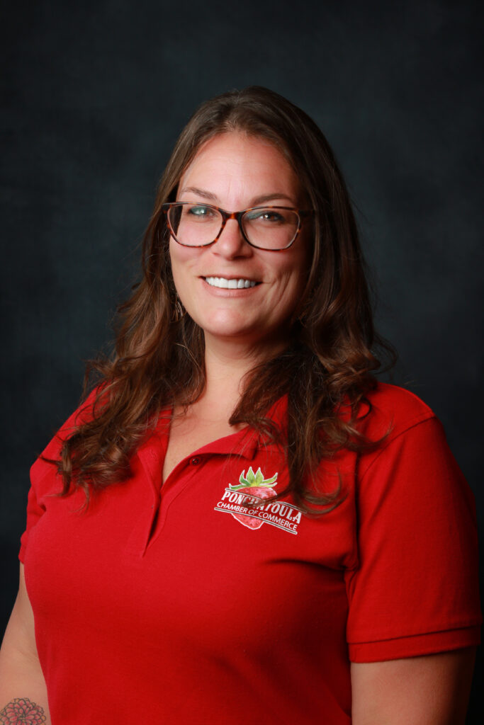 Smiling woman with glasses wearing a red polo shirt featuring a chamber of commerce logo on the chest.
