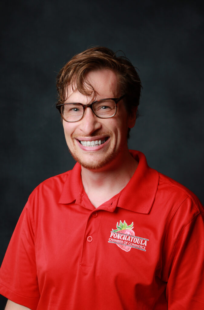 Portrait of a smiling man with glasses, wearing a red polo shirt with a Ponchatoula Chamber of Commerce logo.